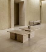 Modern mimari mekân içinde konumlandırılmış, doğal taş dokulu üçlü traverten orta sehpa seti, lüks ve sade iç mekân tasarımı