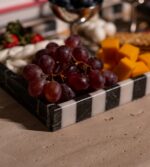 . Siyah beyaz çizgili modern mermer tepside peynir, üzüm, kraker ve meyveler yer alıyor.