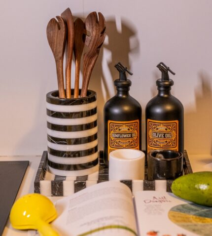 Bir kitap, bir bıçak, bir şişe yemeklik yağ ve modern siyah beyaz çizgili bir vazonun yer aldığı mutfak tezgahı.